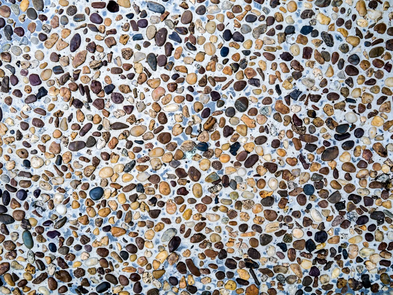 Close-up of exposed aggregate concrete with a mixed brown and cream pebble blend on a light base